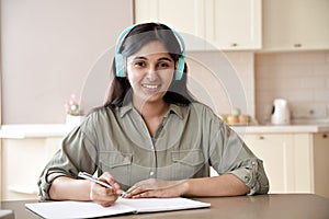 Happy indian girl wear headphones look at camera study at home listen course.