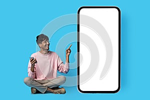 Happy indian guy pointing at huge smartphone with blank screen photo