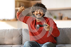 Happy indian guy celebrating win while playing video games at home
