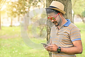 Happy indian guy looking his mobile phone and smiling - Young asian man texting online in park outdoor - New technology trends