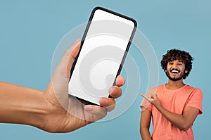 Happy indian guy pointing at huge blank smartphone in giant female hand
