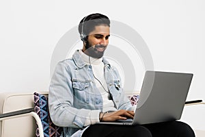 Happy indian man in wireless headphones with laptop computer listening to music at home