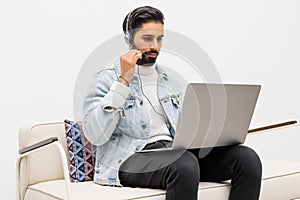 Happy indian man in wireless headphones with laptop computer listening to music at home