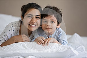 Happy Indian mom and kid lying in white linen