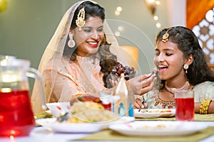 Happy indian mother feeding dates to daughter during ramadan iftar dinner at home - concept of caring mother, ramazan