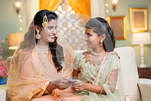 Happy indian muslim mother gifting or giving money to daughter during ramadan festival - concept of savings, finance and