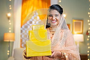 Happy indian muslim woman showing gift boxes by looking at camera at home - concept of festival offer, promotion and