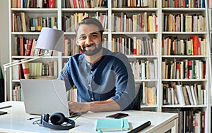 Happy indian professional business man sitting at work with laptop, portrait.