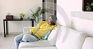 Happy Indian woman get in living room sits on sofa