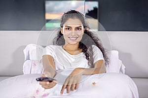 Happy Indian woman watching TV on bed at night