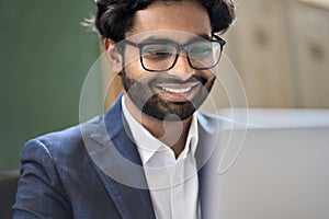 Happy indian young business man executive wearing suit working on laptop.