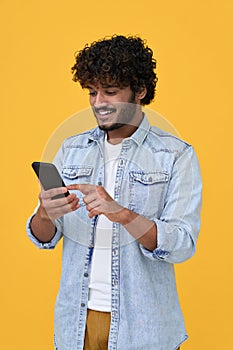 Happy indian young man using cell phone isolated on yellow background.