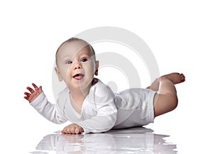 Happy infant baby boy toddler in diaper and white bodysuit is lying on floor on his stomach tummy and waves us