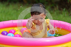 happy infant baby girl playing water splashing with colorful plastic balls in inflatable pool