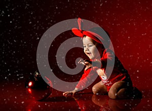 Happy infant baby girl toddler in red bodysuit plays with Christmas New Year fir tree decoration ball under snow