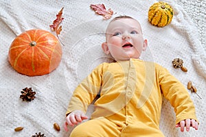 Happy infant baby lies on a blanket in yellow autumn clothes with a red