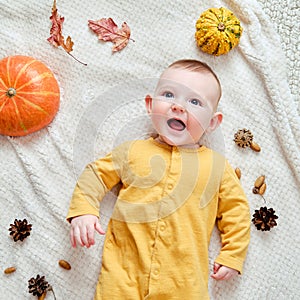 Happy infant baby lies on a blanket in yellow autumn clothes with a red