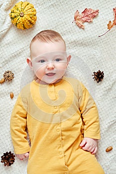 Happy infant baby lies on a blanket in yellow autumn clothes with a red