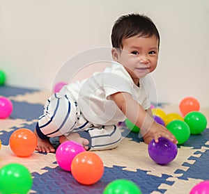 happy infant baby playing colorful balls in playpen