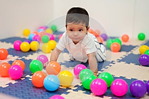 happy infant baby playing colorful balls in playpen