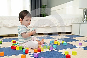 happy infant baby playing wooden block toy on jigsaw mat in bedroom