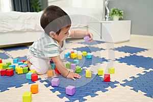 happy infant baby playing wooden block toy on jigsaw mat in bedroom