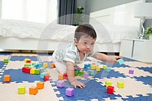 happy infant baby playing wooden block toy on jigsaw mat in bedroom