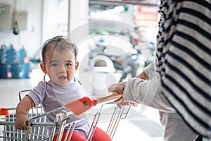 Happy infant baby sitting alone in shopping cart