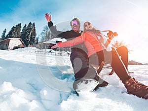 Happy influencers couple having fun with wood vintage sledding on snow high mountains - Young crazy people enoying winter vacation