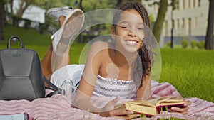 Happy intelligent little girl reading book and smiling at camera. Portrait of joyful African American child with afro