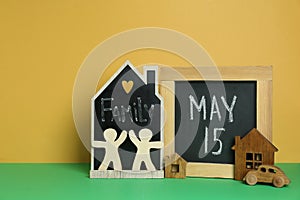 Happy International Family Day. Small chalkboards with text, house models, people figures and toy car on green table against