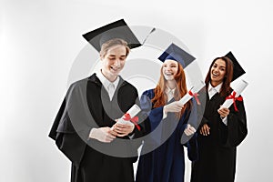 Happy international graduates smiling rejoicing holding diplomas over white background.