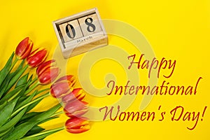Happy International Women`s Day composition bouquet of red tulip buttons, wooden cubic calendar and greeting text. Flat lay from