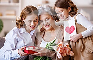 Happy International Women& x27;s Day. daughter and granddaughter giving flowers to grandmother celebrate Mother& x27;s Day