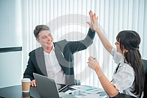 happy interracial businessperson giving high five while working near laptop at workplace, celebrating shared goal achievement,