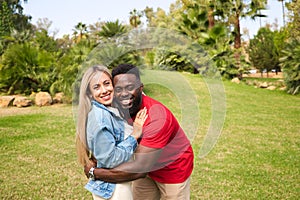 Happy interracial couple hugging in park looking at camera for photo. They are happy and excited