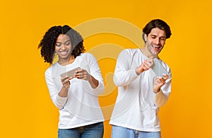 Happy interracial couple playing video games on smartphones, competing each other