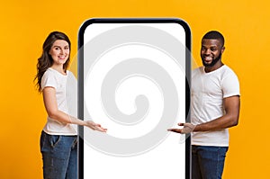 Happy Interracial Couple Pointing At Big Blank Smartphone With White Screen