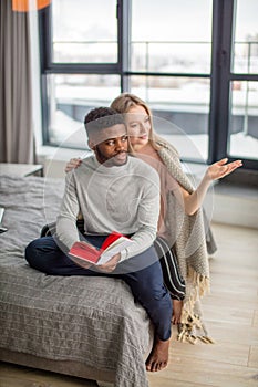 Happy interracial couple spending weekend together at home, relaxing with book