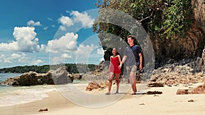 Happy interracial couple walking on the white sand beach shore at summer day.