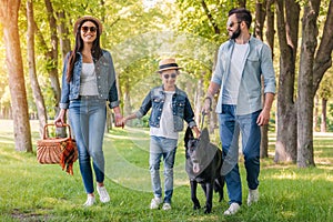 Happy interracial family with picnic basket walking with dog in forest