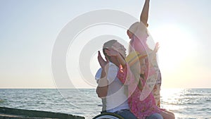 Happy invalid, family play together on background blue sky, girl sitting on daddy in wheelchair with outstretched arms