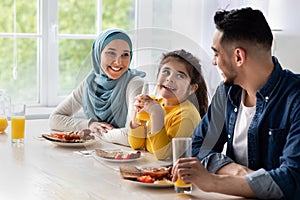 Happy islamic family with little daughter eating tasty breakfast together in kitchen