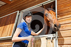 Happy jockey girl stroking horse at riding stable