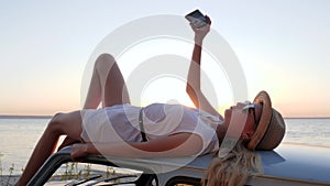 Happy Journey, young woman lying on rooftop auto makes pictures on phone, female make selfie photo at mobile on retro