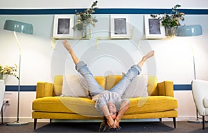 Happy and joyful adult woman lay down on the sofa in reverse position with legs up and head down smiling and having fun at home -