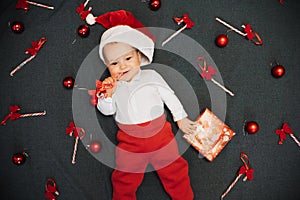 Happy joyful baby boy in Santa Claus hat smiling among Christmas candy canes