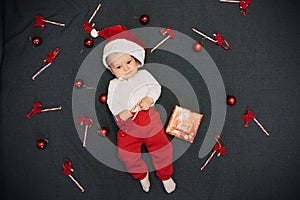 Happy joyful baby boy in Santa Claus hat smiling among Christmas candy canes