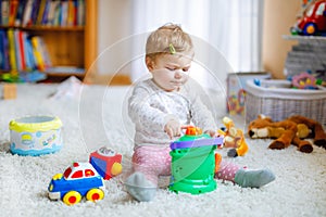 Happy joyful baby girl playing with different colorful toys at home. Adorable healthy toddler child having fun with