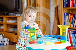 Happy joyful baby girl playing with different colorful toys at home. Adorable healthy toddler child having fun with